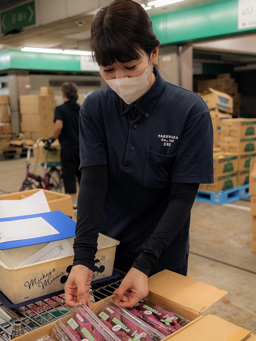 セロリと人参を手に売り場に立つ女性社員。