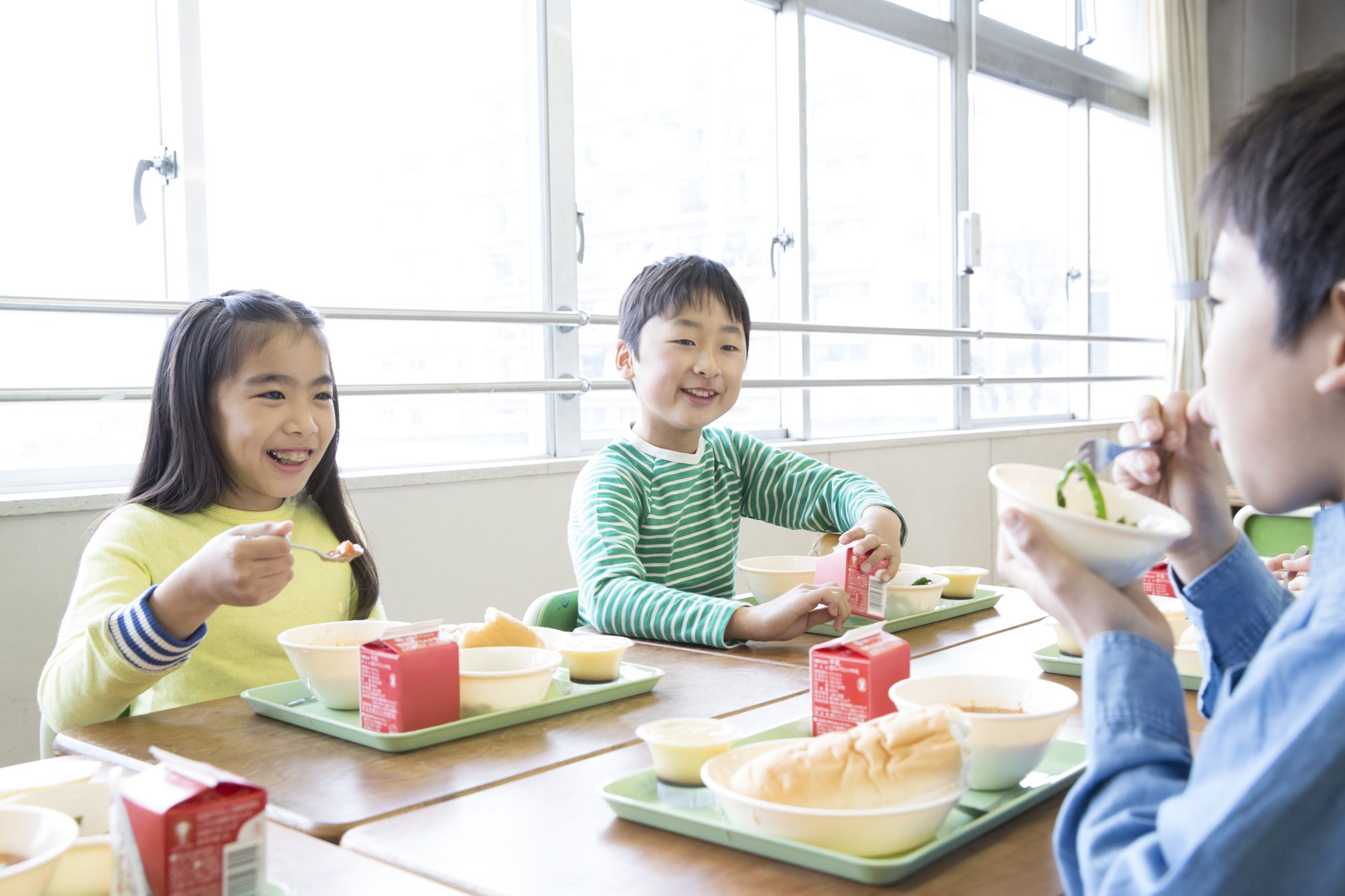 給食を囲んで楽しそうに食べる子どもたち。学校給食の食卓。
